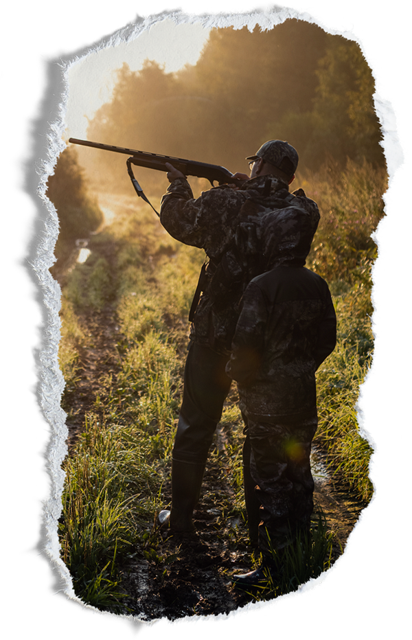 Father and son in camo in a clearing in the woods with father aiming off in the distance
